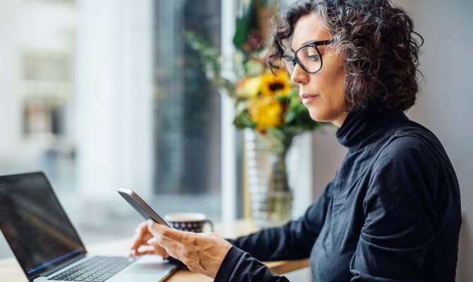 Woman looking at a mobile phone in front of a laptop